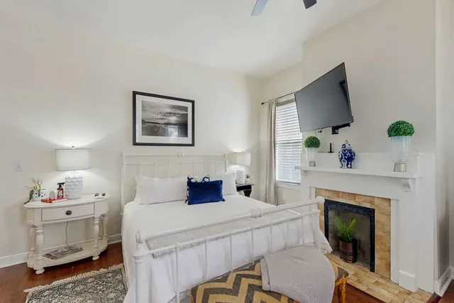 A crisp white iron bed faces a cozy fireplace and vanity in a bedroom at Ola's Oasis in Savannah, GA.