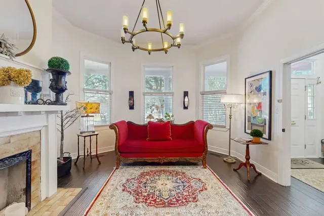 Sunlit front parlor at Ola's Oasis, a whole-home vacation rental in Savannah, GA, with a plush red velvet Victorian sofa beneath a warm chandelier glow.